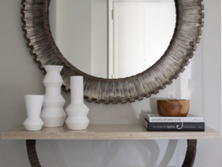 Bronzed round mirror over light stone console table