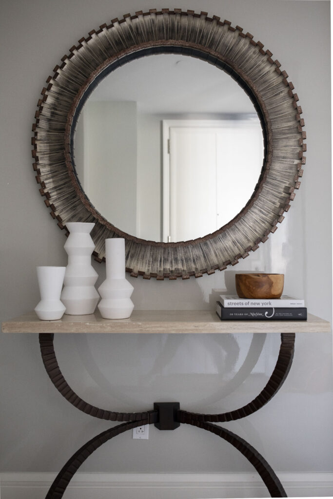 Bronzed round mirror over light stone console table
